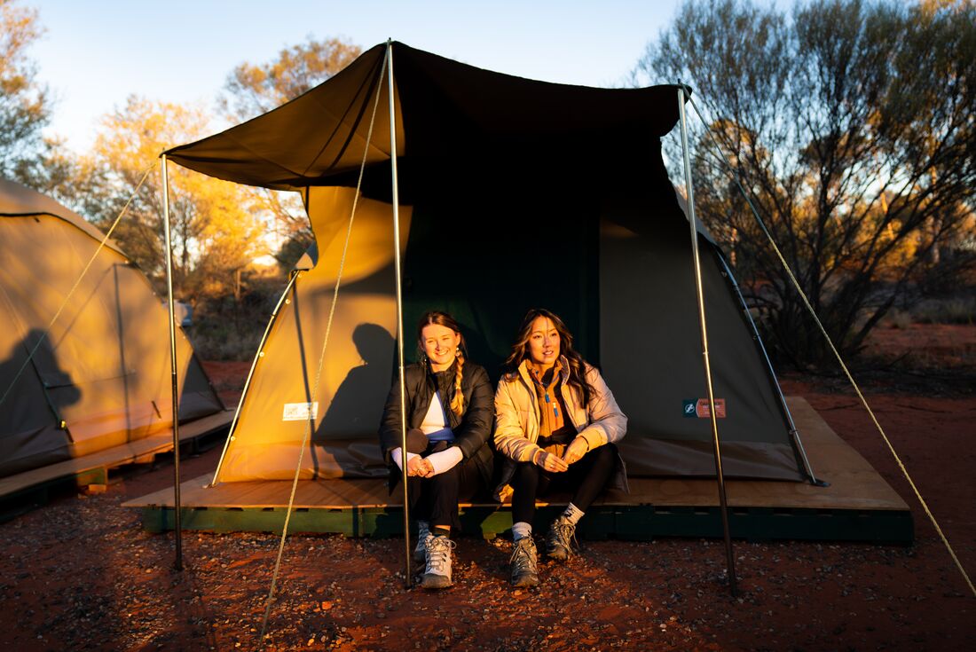Two Intrepid travellers sit at the entrance to a tent set up in the outback
