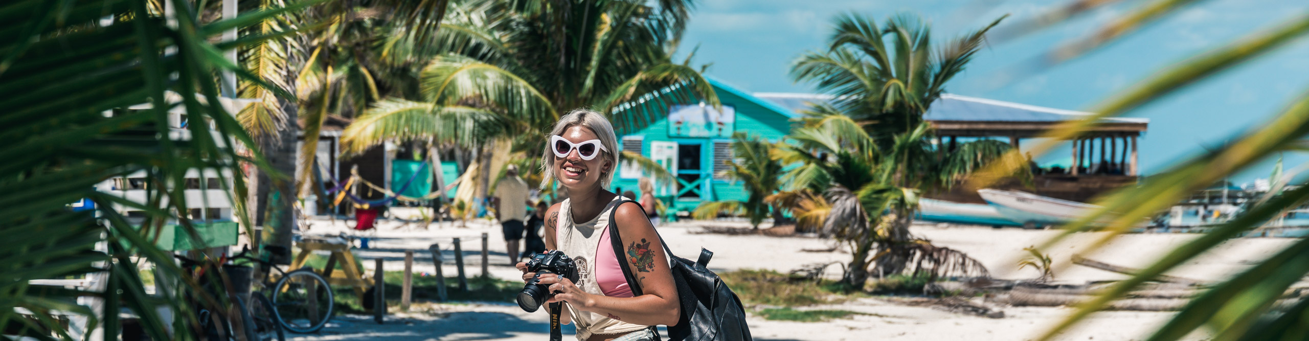 Woman laughing and smiling holding a camera near the beach, surrounded by palm trees, Belize
