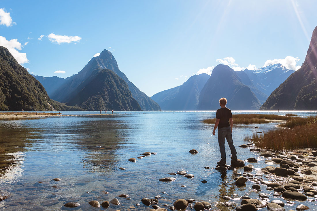 Traveller standing on shore, Milford Sound, Fijordland NP, New Zealand