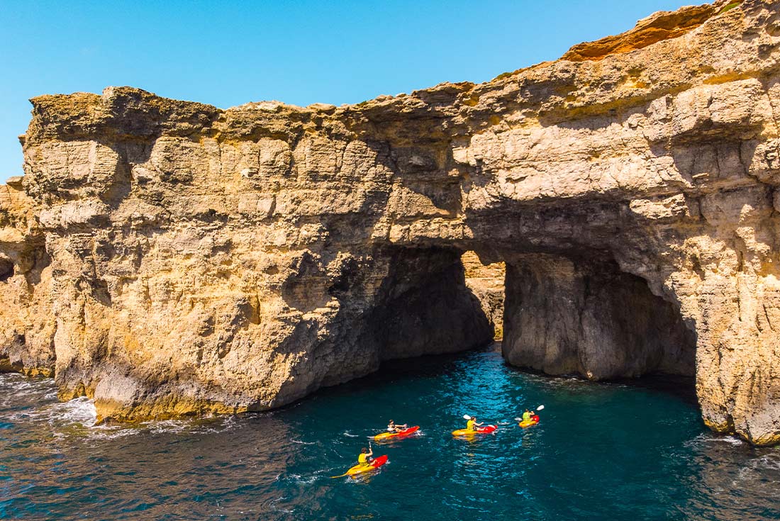 People kayaking under caves on Camino Island, Malta