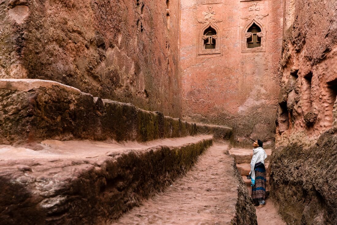 Woman stands looking at the walls of Lalibela Pilgrim 